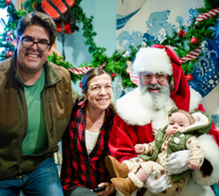 Three adults and a child are smiling together in a festive setting with holiday decorations, including one adult dressed in a Santa Claus costume.

Description generated by AI